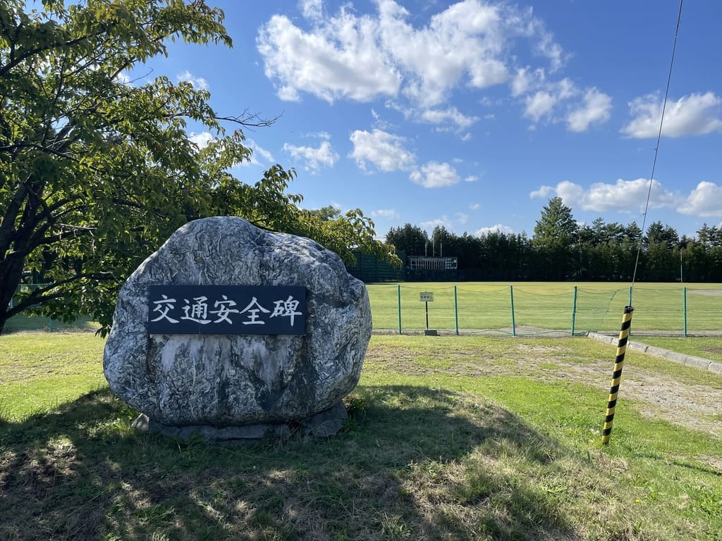 野球場を背景に立つ栗山公園の交通安全碑