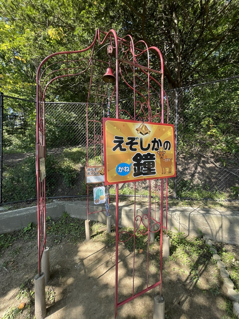 赤い枠に鐘が吊られた栗山公園なかよし動物園のえぞしかの鐘
